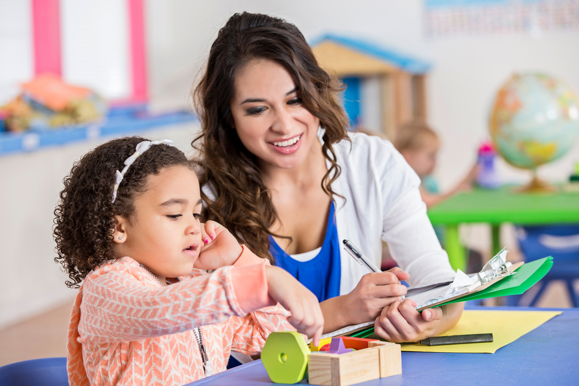 Pretty Hispanic daycare teacher assesses little girl playing blocks