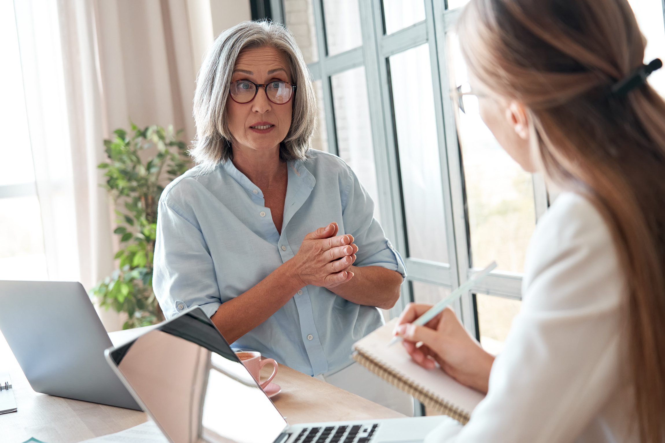 Mature Female Mentor Teacher Talking to Young Intern Student at Office Meeting.